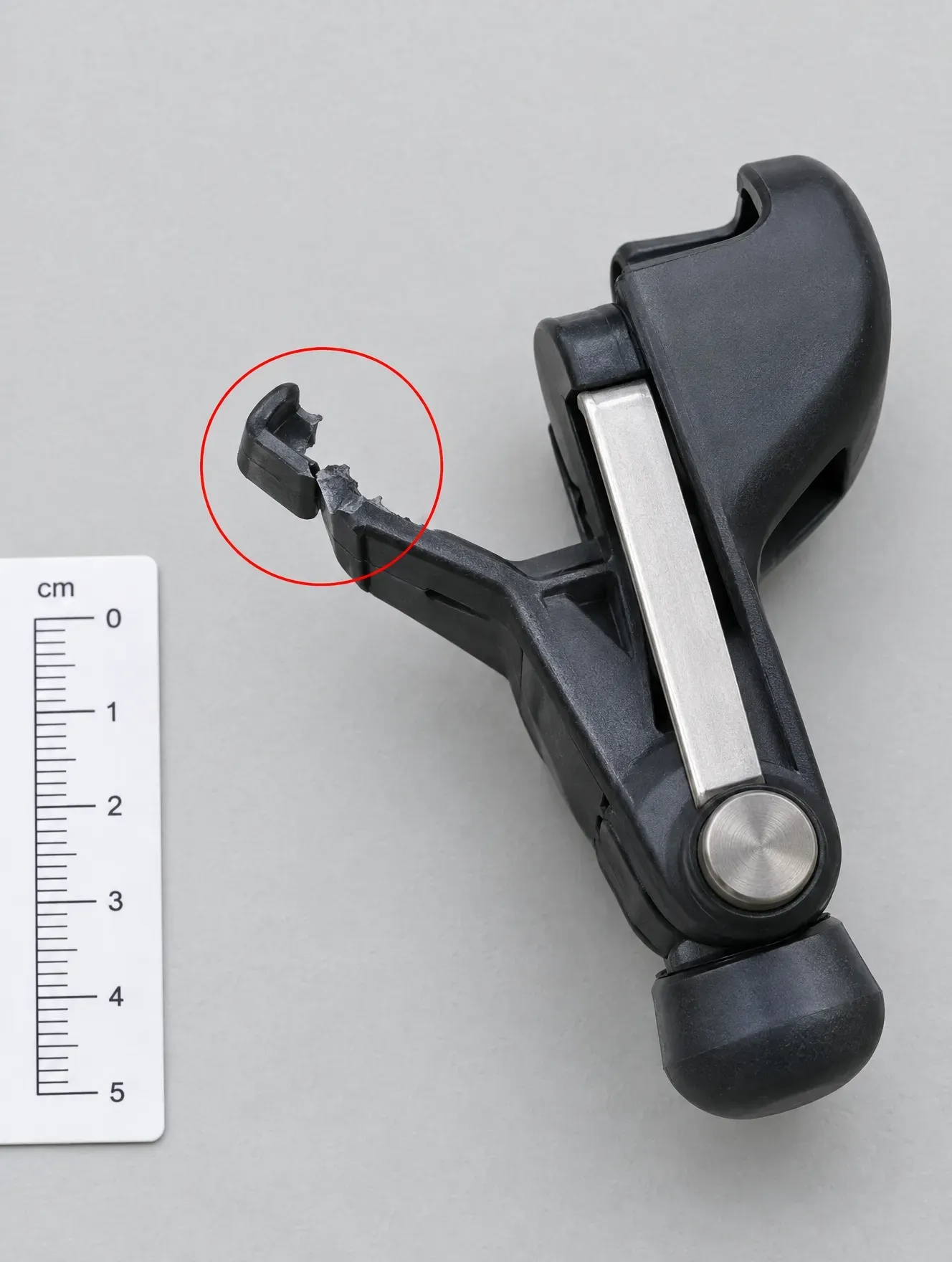 A plastic clip on a product with its tip snapped off, circled in red beside a centimetre ruler