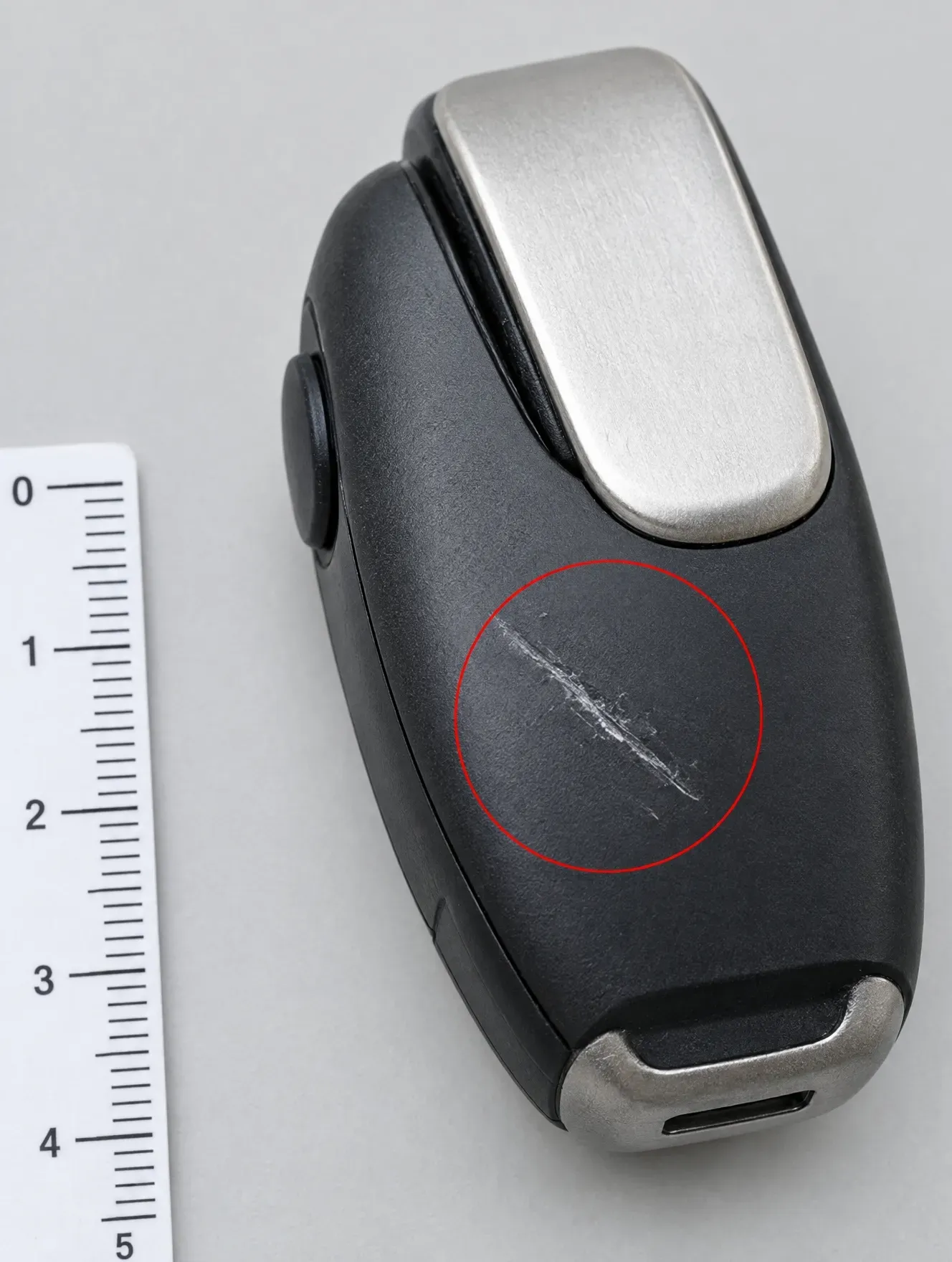 A long scratch across the face of a black plastic product, circled in red beside a ruler