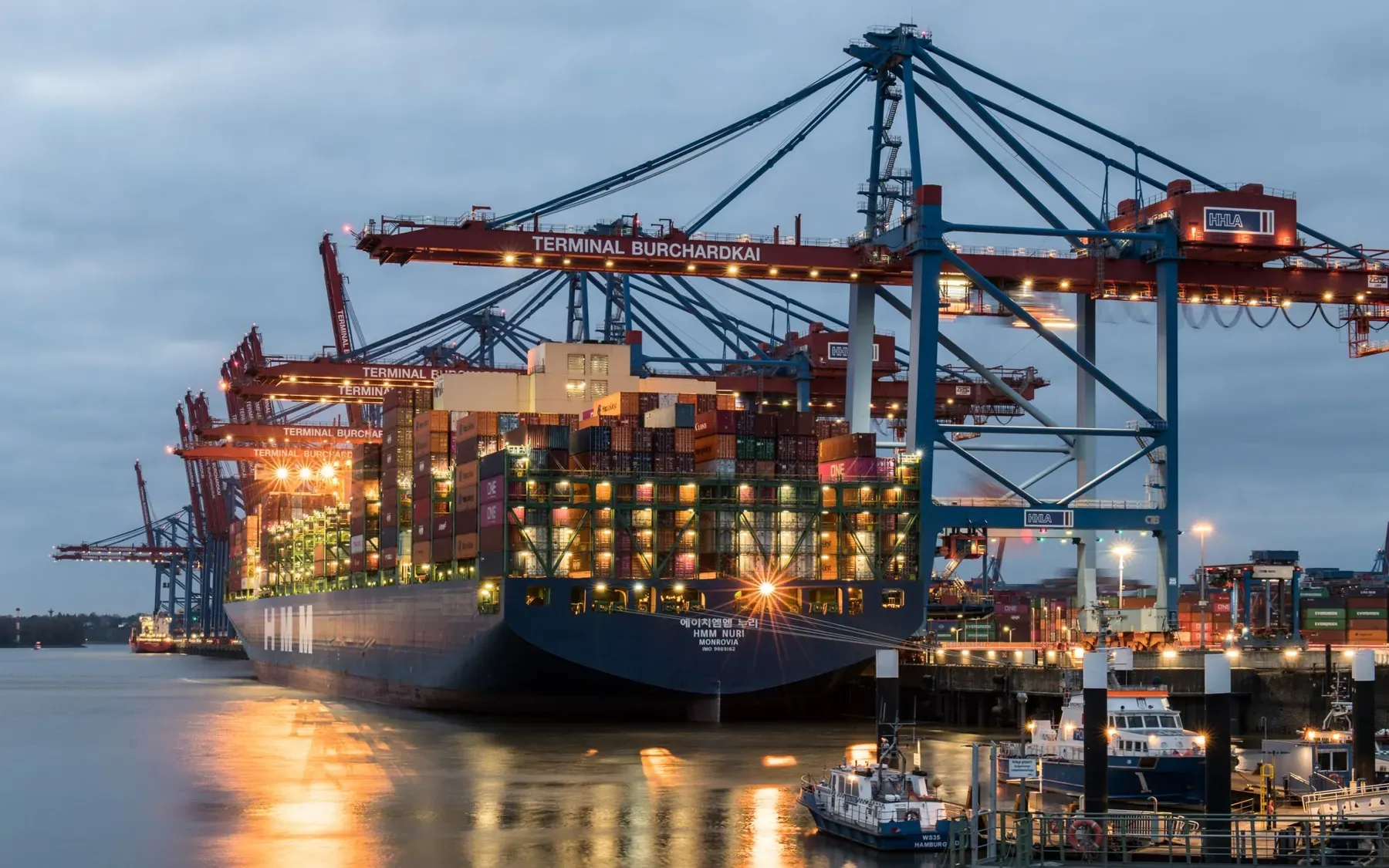 Container ships under gantry cranes at a port terminal in the evening