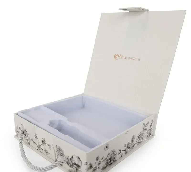 An open white gift box with a floral print, rope handle and fitted insert